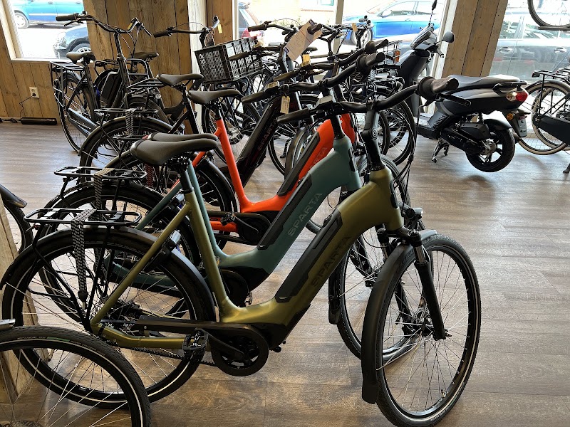 E-bikes van Sparta in groen, oranje en grijs naast een scooter in de showroom.