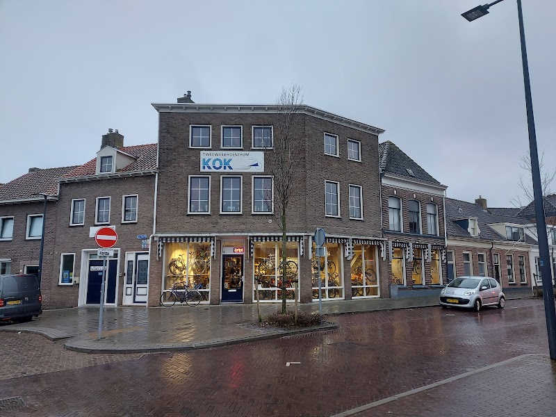 De winkel van Tweewielercentrum Kok op de hoek van De Hagen in Kampen, in de schemer, met verlichte etalages vol fietsen.